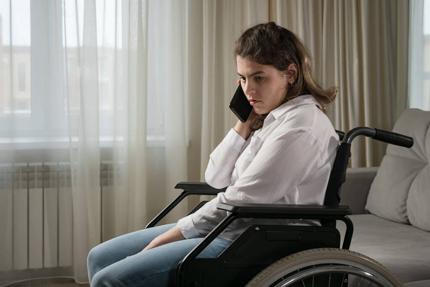 Gehandicapte vrouw in rolstoel gesprekken op mobiele telefoon thuis - Foto, afbeelding