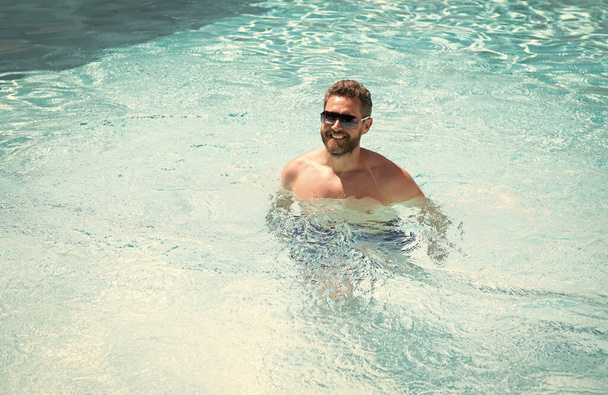счастливый бородатый мужчина в солнцезащитных очках наслаждаться отдыхом в бассейне курортного спа на летних каникулах, летом. - Фото, изображение