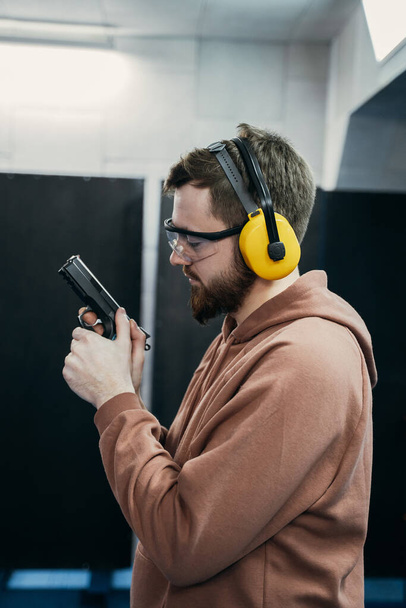 A profile of the face of a serious man who holds a short-barreled weapon in his hands and looks at the target before being fired. shooting range - Φωτογραφία, εικόνα