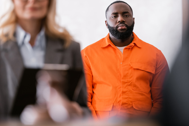 african american man in orange jail uniform near advocate on blurred foreground - Foto, Bild