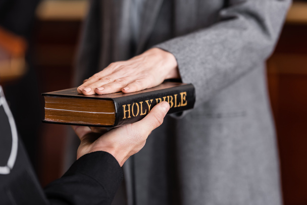 частичный взгляд судебного пристава, держащего Библию рядом с женщиной, дающей клятву в суде - Фото, изображение