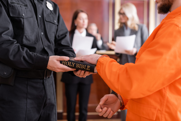 Gerichtsvollzieher in Uniform hält Bibel in der Nähe des Angeklagten und leistet vor Gericht Eid - Foto, Bild