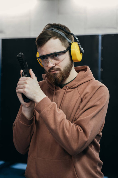 A man takes aim at a target before firing a pistol. special outfit - ballistic headphones. - Zdjęcie, obraz