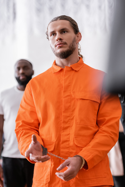 bearded man in handcuffs and orange jail uniform gesturing in courtroom - Foto, imagen
