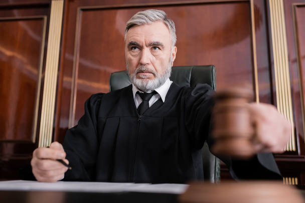 senior judge in mantle holding blurred gavel while sentencing in court - Fotoğraf, Görsel