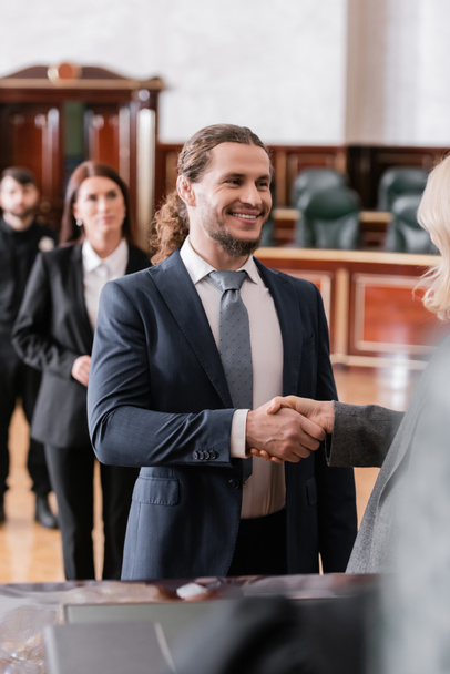 cheerful businessman shaking hands with blurred attorney in courtroom - Photo, Image