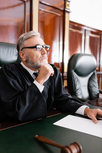 senior judge in robe and eyeglasses sitting with pen during litigation - Zdjęcie, obraz