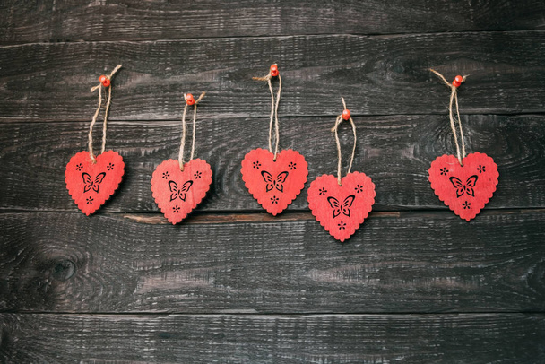 Κρεμαστά ξύλινα κόκκινα καρδιές σε ξύλινο τοίχο στη σειρά. - Φωτογραφία, εικόνα