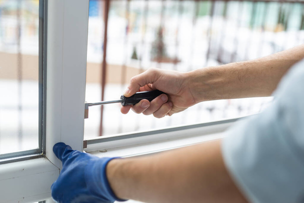 Ένας εργάτης με γάντια ρυθμίζει την εγκατεστημένη πλαστική πόρτα - Φωτογραφία, εικόνα