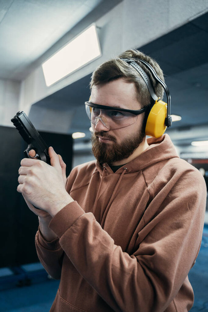 A serious man holds a short-barreled weapon in his hands and looks at the target before firing. Shooting range - Foto, Bild