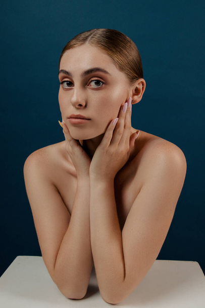 Young girl, woman with clean perfect skin. Isolated girl in studio.  Fashion close up Portrait of beauty model with natural nude make up and long eyelashes. Blue solid background. Hand poses - Fotoğraf, Görsel