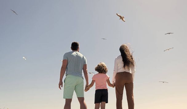 семья отца и ребенка, глядя в будущее, держатся за руки летом, вид сзади, летние каникулы. - Фото, изображение