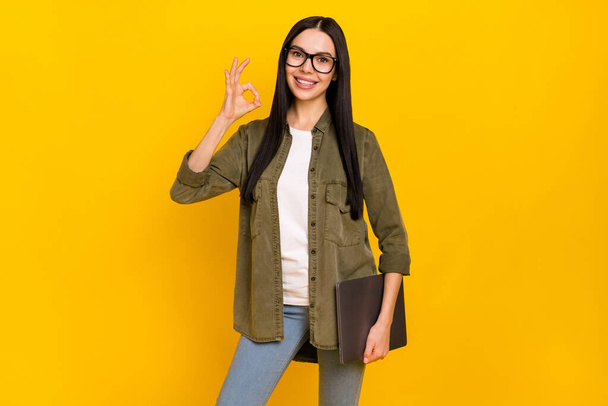 Photo of funny millennial lady hold laptop show okey wear spectacles shirt isolated on yellow background - Foto, Imagem