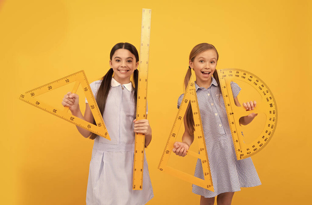 Happy school age children hold geometric tools for geometry lesson yellow background, schooling - Photo, Image