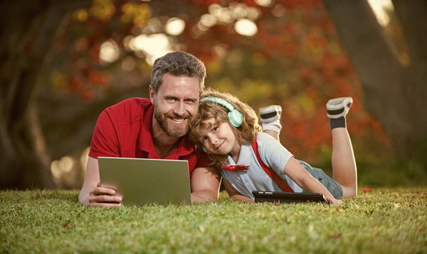 happy family of dad and son use laptop for lesson listen music in headphones in park, happiness. - Photo, Image