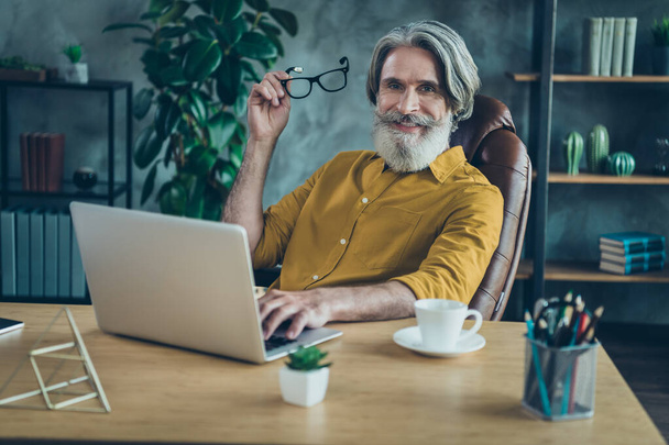 Photo of cheerful mature guy dressed yellow shirt spectacles chatting modern gadget indoors workplace workstation. - Fotoğraf, Görsel