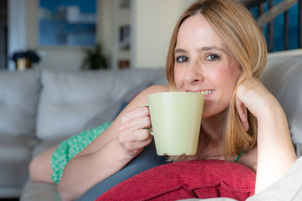 Bela jovem caucasiana desfrutando de uma xícara de café enquanto relaxa em casa. - Foto, Imagem