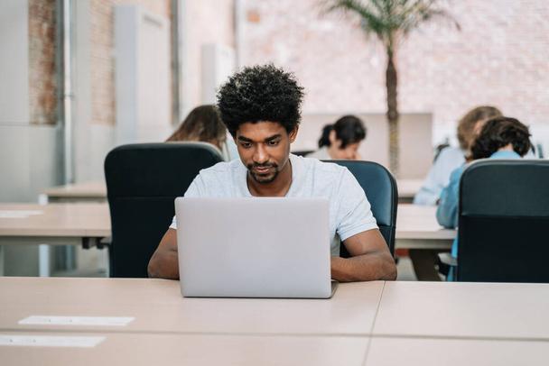 Zelfverzekerde zwarte man werkt op de computer in een ruim modern kantoor - Foto, afbeelding