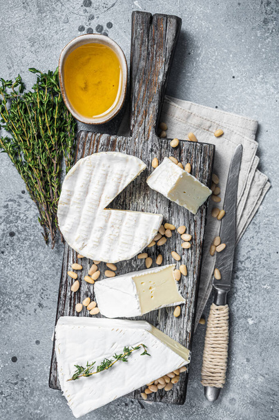Вкусный сыр бри и камамбер на деревянной доске с травами и орехами. Молочные французские продукты. Серый фон. Вид сверху - Фото, изображение