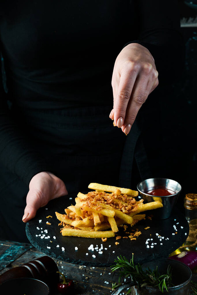 Fast food, french fries. Potatoes with bacon on a plate in the hands of a chef, on rustic wooden background. Fast food concept. - Foto, Imagem