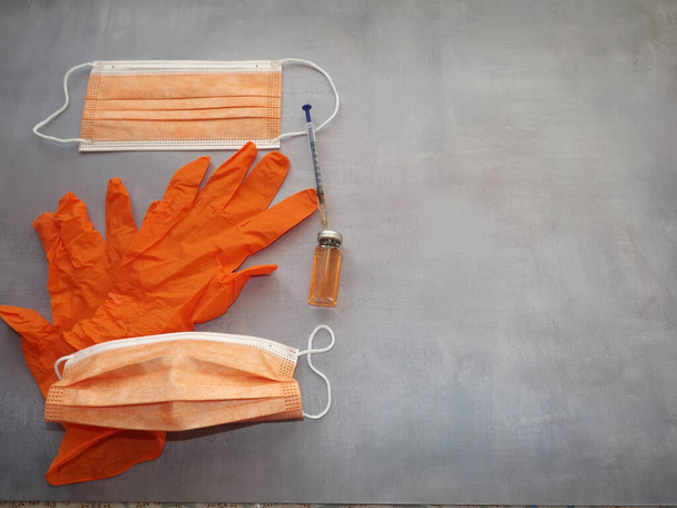 на сером фоне, вакцина, шприц, оранжевые медицинские маски и перчатки - Фото, изображение