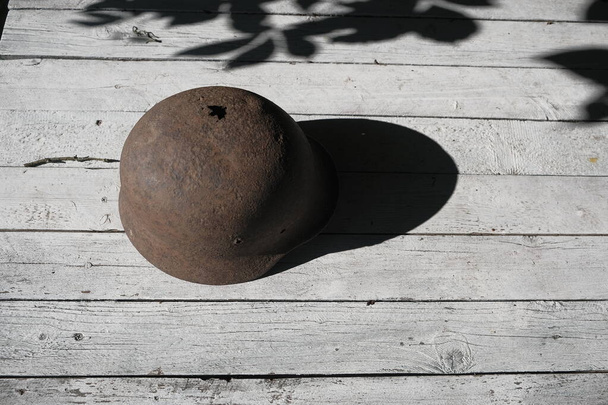 Denk aan de oorlog! Een roestige Duitse helm uit de Tweede Wereldoorlog, doorboord door een kogel, op een witte tafel verlicht door de zon - Foto, afbeelding