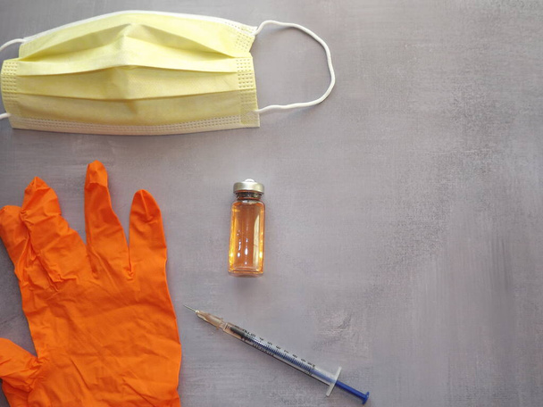 na šedém pozadí, vakcína, injekční stříkačka, oranžové lékařské masky a rukavice - Fotografie, Obrázek