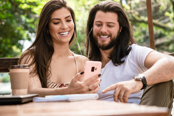 公園内のヘッドフォン付き携帯電話でビデオを見ているブラジルのカップル - 写真・画像