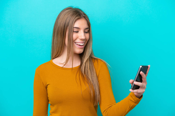 Молодая белая женщина, изолированная на синем фоне, отправляет сообщение или электронную почту с мобильным телефоном - Фото, изображение