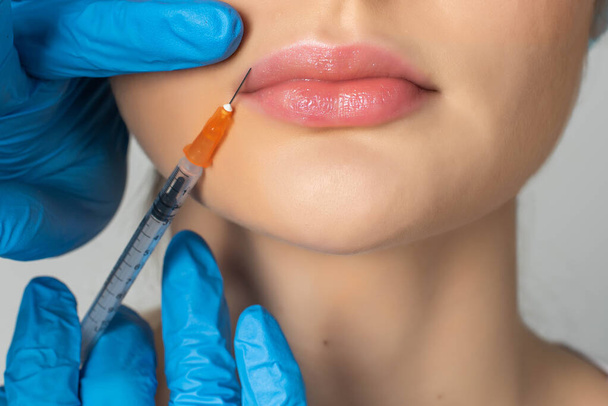 Profesjonalny kosmetolog wstrzykujący silikon w usta. Zbliżenie kobiety otrzymującej wstrzyknięcie botoksu w usta. - Zdjęcie, obraz