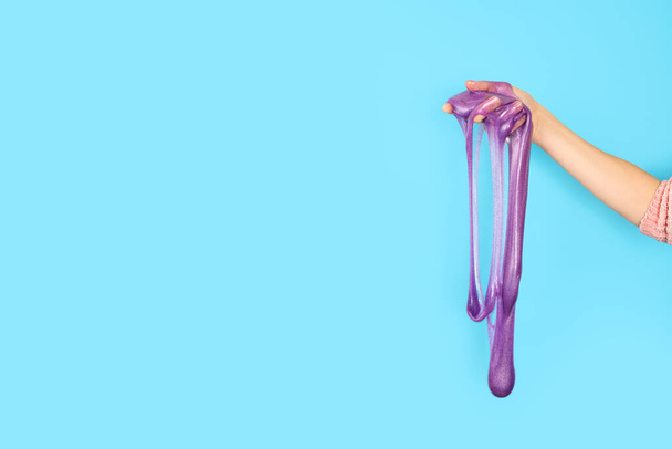 Close-up op glanzend paars of violet slijm in de hand geïsoleerd op blauwe achtergrond. Plezier en stress verlichting concept. Banner met kopieerruimte - Foto, afbeelding