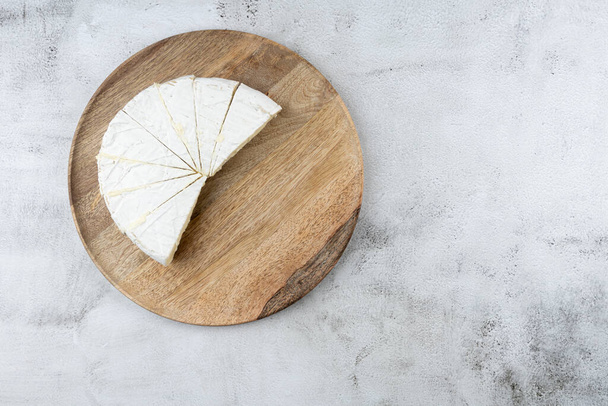 Vista superior, queso blanco redondo en rodajas: un producto lácteo cremoso tradicional en una placa de madera. HOME, Estilo de país - Foto, imagen
