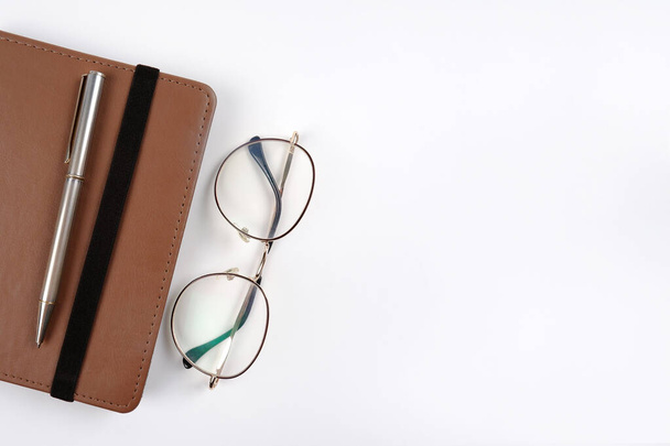 An e-book in a brown case or a notebook with round stylish optical glasses, a pen on a white background.The concept of reading, planning, making a to-do list, convenient gadgets.Copyspace - Φωτογραφία, εικόνα