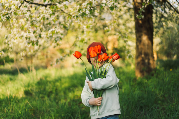 Весела щаслива дитина з тюльпанами квітковий букет на природі
. - Фото, зображення