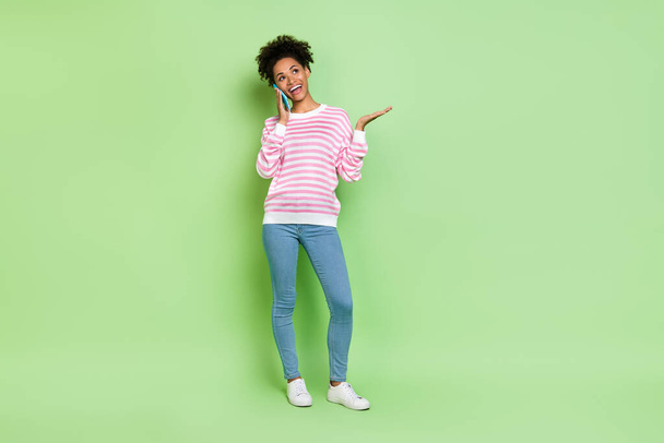 Photo of cheerful friendly lady hold phone have carefree conversation wear striped shirt isolated green color background - Fotoğraf, Görsel