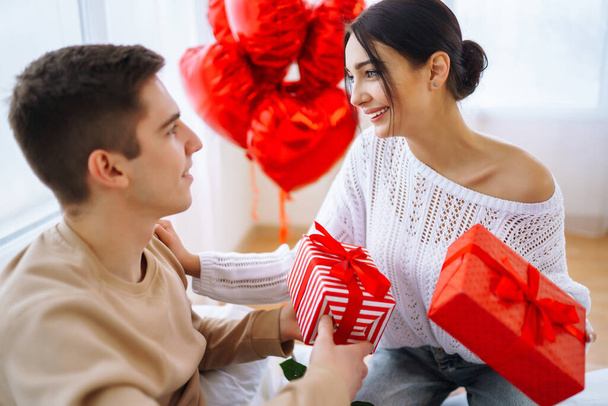 Valentine's Day concept. Lovers give each other gifts. Young couple at home celebrating Valentine's Day. - Фото, изображение