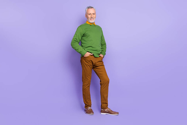 Photo of charismatic retired man wear green sweater walking hands arms pockets isolated violet color background - Valokuva, kuva
