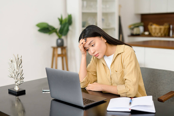 Sad asian woman looking annoyed and stressed, sitting at the desk, using a laptop, thinking, feeling tired and bored - Fotoğraf, Görsel