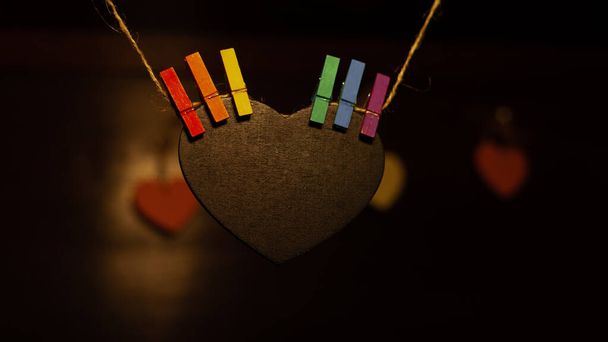 wooden heart hanging from a rope and gripped with tweezers with LGBT colors - Photo, Image