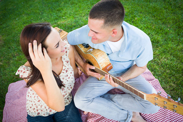 Молодий дорослий чоловік грає гітару для своєї дівчини в парку
. - Фото, зображення
