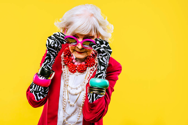Happy and funny cool old lady with fashionable clothes portrait on colored background - Youthful grandmother with extravagant style, concepts about lifestyle, seniority and elderly people - Photo, Image