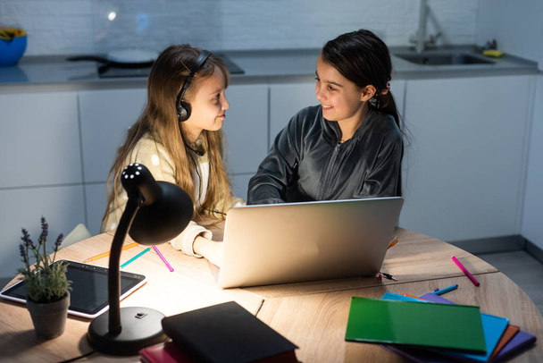 Δύο παιδιά κορίτσια μαθητές σπουδάζουν σε απευθείας σύνδεση με το δάσκαλο με βιντεοκλήση μαζί. Αδέρφια homeschooling με φορητό υπολογιστή κατά τη διάρκεια της καραντίνας λόγω πανδημίας Covid 19. - Φωτογραφία, εικόνα