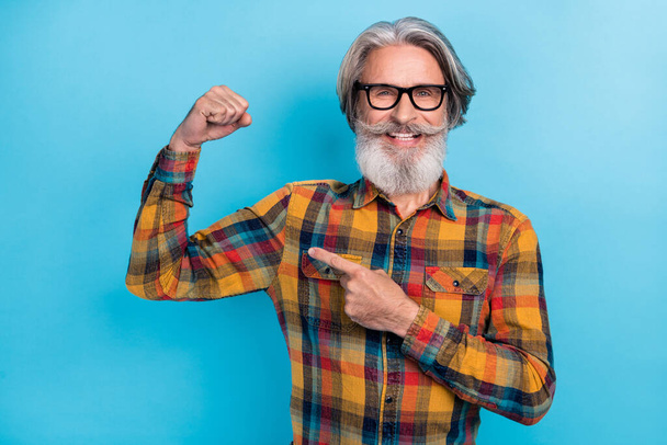 Photo of funny confident retired man wear plaid shirt spectacles pointing finger arm muscle isolated blue color background - Foto, immagini