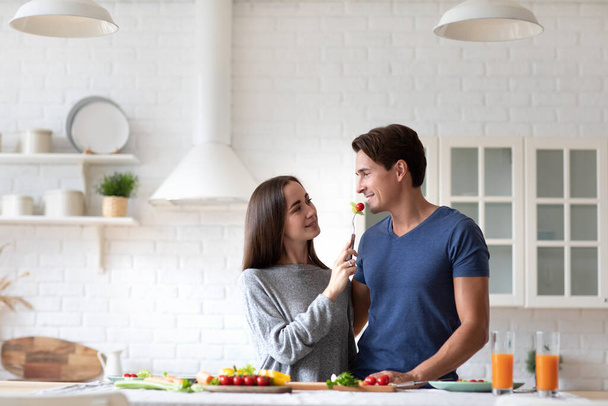 Beautiful young couple looks at each other and smiles while eating in the kitchen. Healthy eating, spending time at home together. - Fotoğraf, Görsel