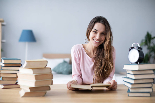 Smiling female student with a pile of books looks at the camera. Concept of home or distance learning. - Φωτογραφία, εικόνα