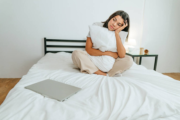 Yatakta dizüstü bilgisayarla oturan genç bir kadın. - Fotoğraf, Görsel