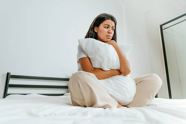 Young woman sitting on the bed looking sad - Фото, зображення