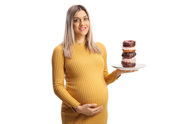 Pregnant woman holding a plate with chocolate donuts and smiling isolated on white background - Фото, изображение