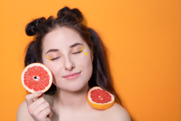 γλυκιά χαρούμενη μελαχρινή γυναίκα κορίτσι θηλυκό με περικοπή φέτα γκρέιπφρουτ κοντά στο πρόσωπο του δέρματος σε πορτοκαλί φόντο. νόστιμο ζουμερό φρούτο. Τροπικά εσπεριδοειδή, υγιεινή διατροφή. απώλεια βάρους - Φωτογραφία, εικόνα