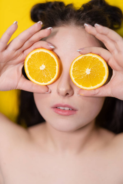 mladá brunetka žena dívka s plátkem pomerančového ovoce v blízkosti kůže tvář na žlutém pozadí. chutné šťavnaté ovoce. Tropické ovoce, zdravé jídlo. Citrusový plátek. chutné šťavnaté ovoce - Fotografie, Obrázek